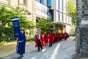 Image shows graduating students walking in a line outside of Myhal Centre.