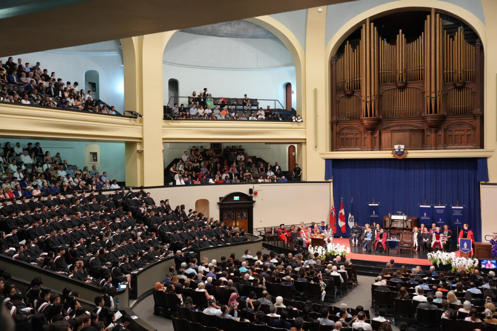 Photo shows graduating students seated inside Convocation Hall.